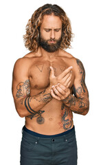 Handsome man with beard and long hair standing shirtless showing tattoos suffering pain on hands...