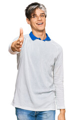 Fototapeta premium Young hispanic man wearing casual clothes smiling friendly offering handshake as greeting and welcoming. successful business.