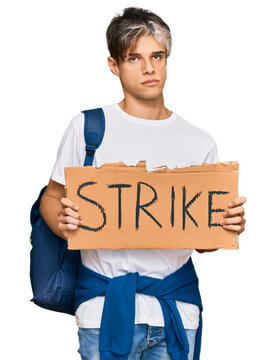 Young hispanic man holding strike banner cardboard thinking attitude and sober expression looking self confident