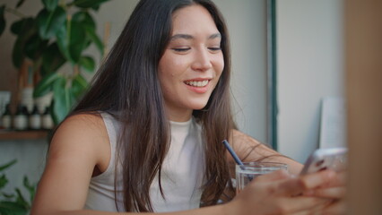 Smiling student messaging cellphone in cafe close up. Happy thai woman browsing