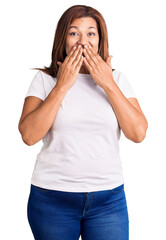 Middle age latin woman wearing casual white tshirt laughing and embarrassed giggle covering mouth...