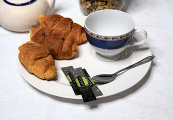 Breakfast with a white and blue cup along with two small croissants, cereals and matcha tea.