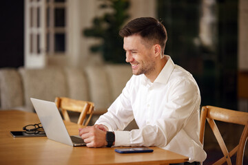 A professional gentleman smiles subtly as he interacts with a laptop at a polished wooden table,...