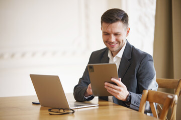 A jovial executive in a tailored suit jacket and white shirt beams as he peruses his tablet, with a...