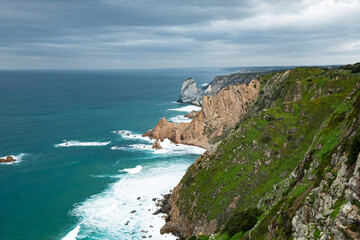 Fototapeta na wymiar Dramatic coastal cliffs tower over the churning blue waters of the ocean, showcasing nature's wild beauty under a cloudy sky. 