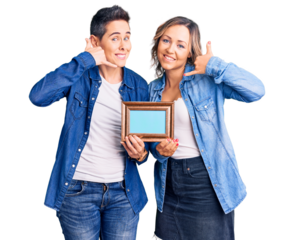 Couple of women holding empty frame smiling doing phone gesture with hand and fingers like talking on the telephone. communicating concepts.