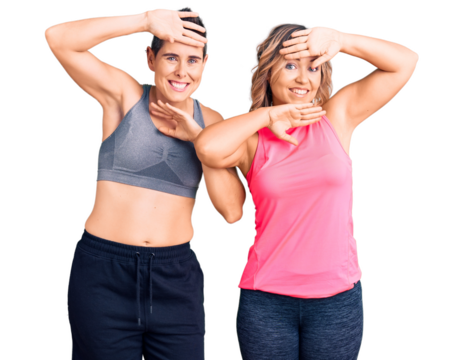 Couple of women wearing sportswear smiling cheerful playing peek a boo with hands showing face. surprised and exited