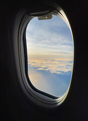 View from an airplane window. Clouds and sunny sky at sunrise from up above. Porthole in a aircraft.