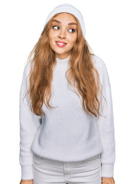 Young caucasian girl wearing wool sweater and winter cap smiling looking to the side and staring away thinking.