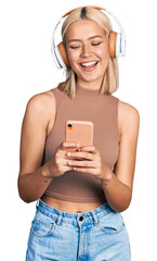 Beautiful young blonde woman using smartphone wearing headphones smiling and laughing hard out loud...