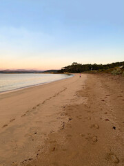Sunrise on a beach. Dawn on the beach. Ocean view at low tide. Waves curling on the shore. Beach and mountains at sunset. Woman walking on sand in the distance.