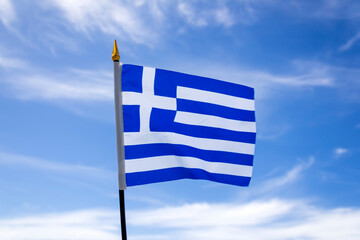 Greek national flag fluttering in the wind  in front of blue sky with white clouds