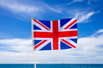 Flag of the United Kingdom fluttering in front of blue sky with white clouds and sea