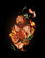 Fried beef steaks with rosemary and garlic on fire close-up on black background - obrazy, fototapety, plakaty