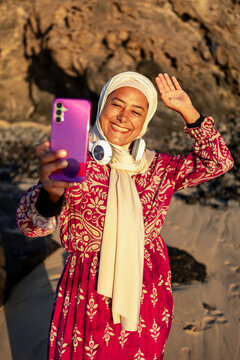Smiling Muslim Woman with Smartphone on the Beach