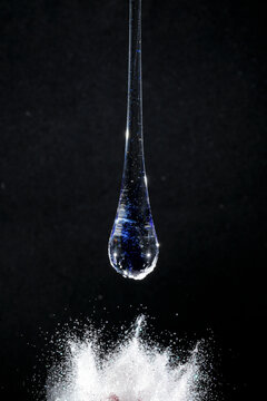 Gota de vidro azul semi transparente em fundo preto. Fotografia em close up de uma pe&ccedil;a similar a um l&iacute;quido de alta viscosidade pingando em cima de glitter branco.