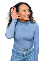 Young hispanic woman with curly hair wearing casual clothes smiling with hand over ear listening an...