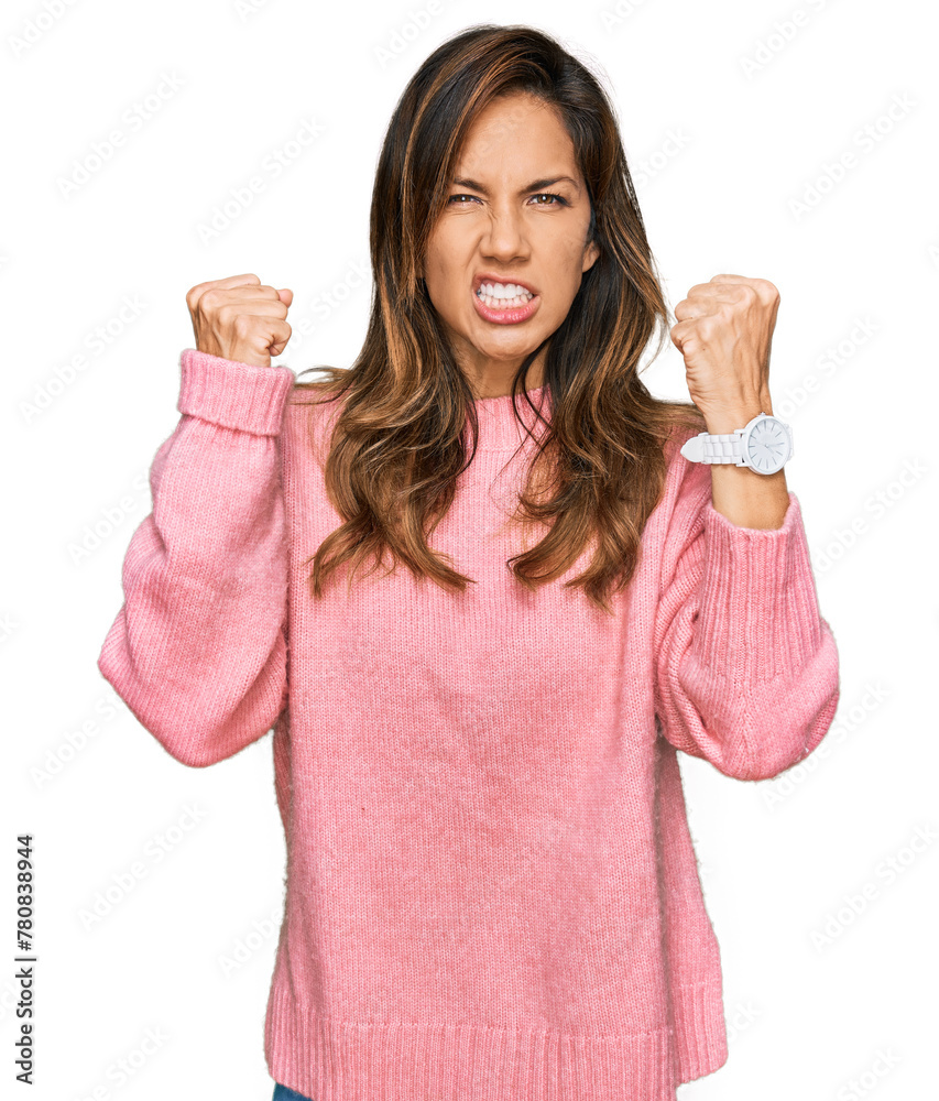 Wall mural Young hispanic woman wearing casual clothes angry and mad raising fists frustrated and furious while shouting with anger. rage and aggressive concept.