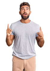Young hispanic man wearing casual clothes amazed and surprised looking up and pointing with fingers...