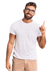 Young hispanic man wearing casual clothes and glasses pointing finger up with successful idea. exited and happy. number one.