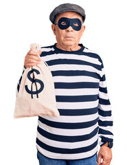 Senior handsome man wearing burglar mask holding money bag thinking attitude and sober expression...