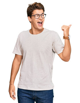 Handsome caucasian man wearing casual clothes and glasses smiling with happy face looking and pointing to the side with thumb up.
