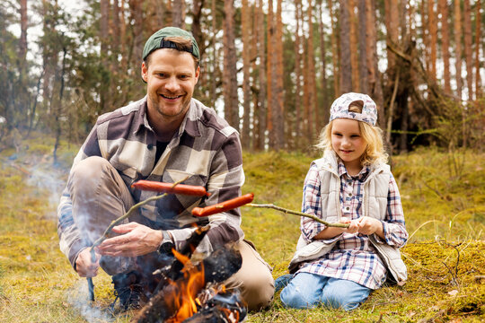 father and daughter spend time together and frying sausages over a bonfire while camping in forest. bonding activities