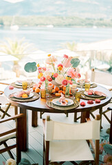 Round festive table with bouquets of flowers and plates on wicker rugs on the terrace overlooking...