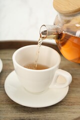 Pouring aromatic tea in cup at table, closeup