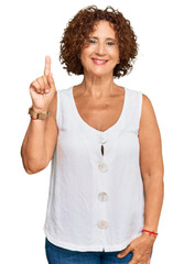 Beautiful middle age mature woman wearing casual white shirt showing and pointing up with finger number one while smiling confident and happy.