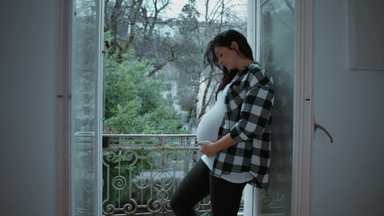 Pregnant Mother Tenderly Caressing Her 8-Month Belly by Apartment Balcony, Radiating Love and Affection While Expecting Newborn Baby