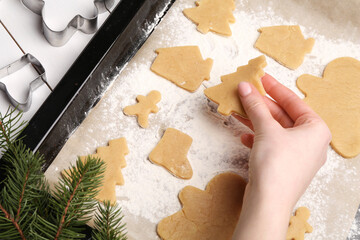 Woman putting raw Christmas cookies on baking tray at white table, closeup