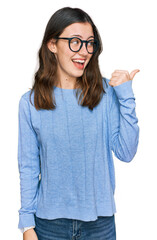 Young beautiful woman wearing casual clothes and glasses smiling with happy face looking and pointing to the side with thumb up.