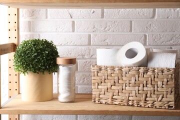 Toilet paper rolls in wicker basket, floral decor and cotton pads on wooden shelf against white...