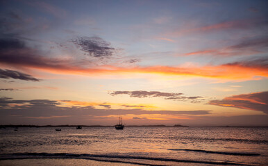 Pôr-do-sol na linha do mar, com barcos e navios no horizonte e degradê colorido de nuvens no...