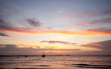 P&ocirc;r-do-sol na linha do mar, com barcos e navios no horizonte e degrad&ecirc; colorido de nuvens no nordeste brasileiro. C&eacute;u alaranjado e roxo. 