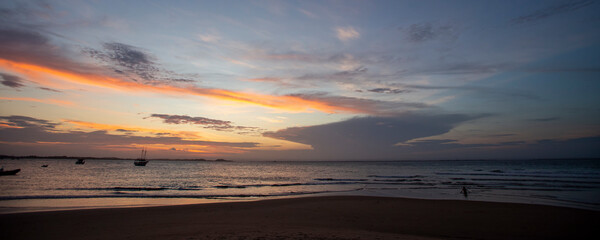 Fototapeta na wymiar Pôr-do-sol na linha do mar, com barcos e navios no horizonte e degradê colorido de nuvens no nordeste brasileiro. Céu alaranjado e roxo. 
