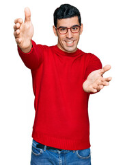 Handsome hispanic man wearing casual clothes and glasses looking at the camera smiling with open arms for hug. cheerful expression embracing happiness.