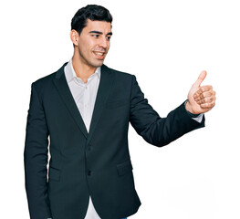 Handsome hispanic man wearing business clothes looking proud, smiling doing thumbs up gesture to the side