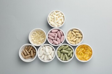 Different vitamin pills in bowls on grey background, flat lay