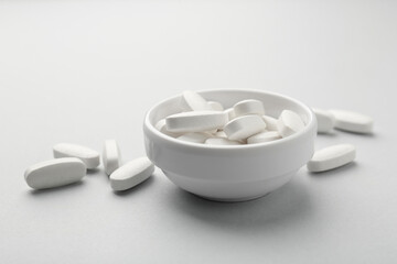 Vitamin pills in bowl on grey background, closeup