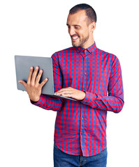 Young handsome man working using computer laptop looking positive and happy standing and smiling...