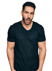 Obraz premium Hispanic man with beard wearing casual black t shirt afraid and shocked with surprise expression, fear and excited face.