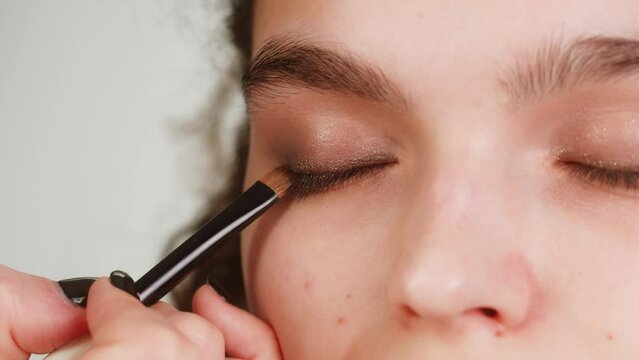 Eye shadow makeup to the upper eyelid, close-up. Makeup artist applies a bright eye shadow with a make-up brush.Tutorial master class of professional makeup, smoky eyes 