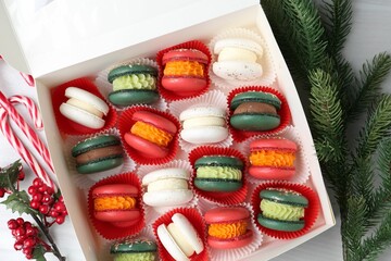 Different tasty Christmas macarons in box and festive decor on white table, flat lay