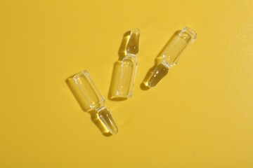 Naklejka premium Glass ampoules with liquid on yellow background, flat lay