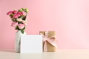 Happy Mother's Day. Gift box, blank card and bouquet of beautiful flowers in vase on white table against pink background. Space for text - obrazy, fototapety, plakaty