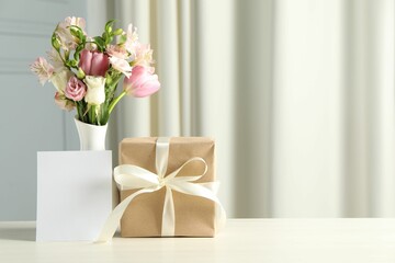 Happy Mother's Day. Gift box, blank card and bouquet of beautiful flowers in vase on white table indoors. Space for text
