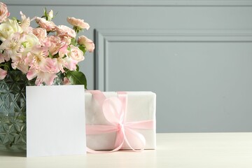 Happy Mother's Day. Gift box, blank card and bouquet of beautiful flowers in vase on white table...