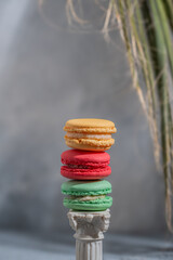 Colored macarons on a decorative column. The background with a palm branch is blurred. Side view.